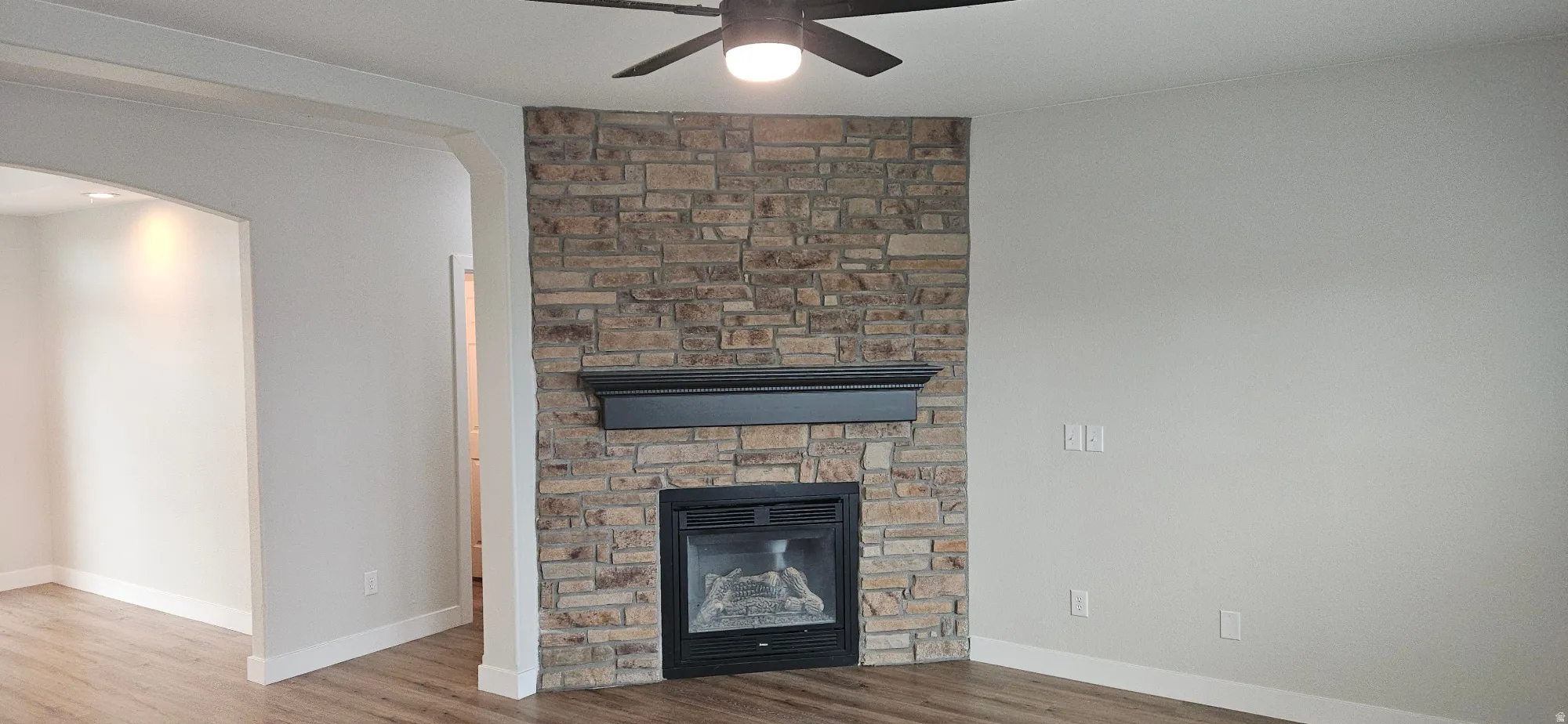 Detailed view of a stone fireplace, ceiling fan, wood finished floors, and arched walkways