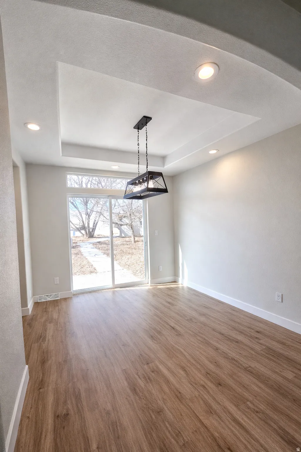 Unfurnished dining area with a raised ceiling, wood finished floors, and recessed lighting