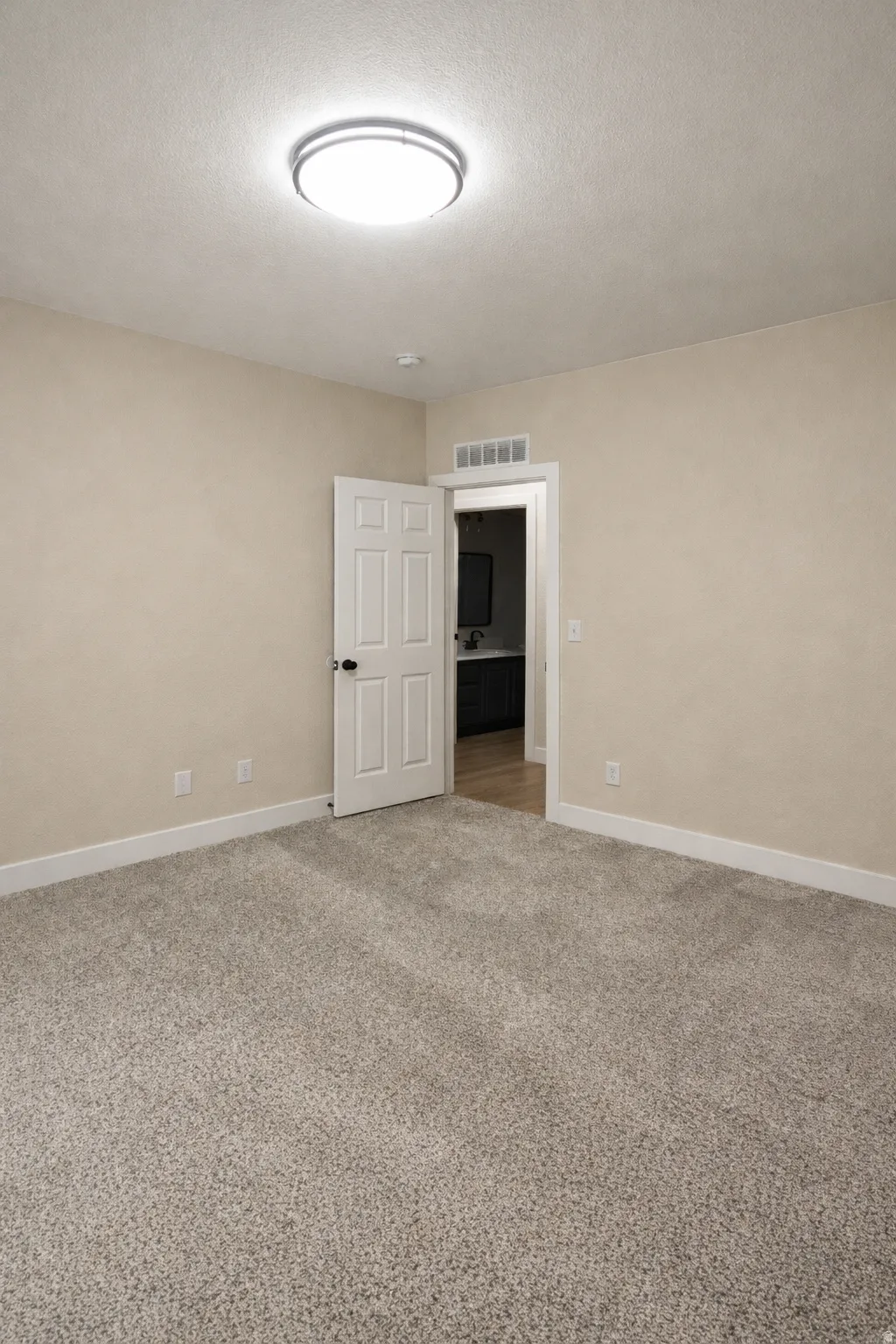 Empty room with light colored carpet and a textured ceiling