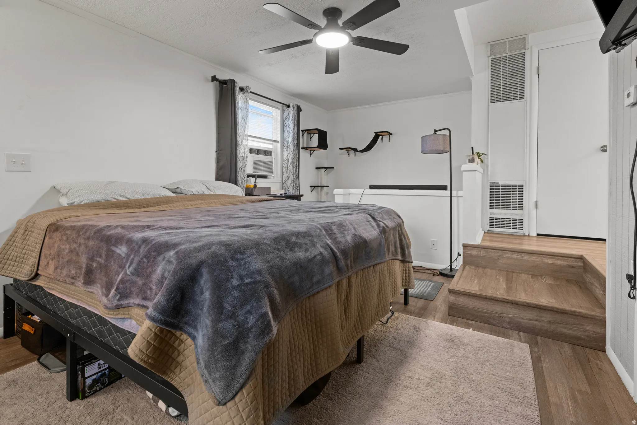 Bedroom with wood finished floors, a heating unit, a ceiling fan, a textured ceiling, and cooling unit