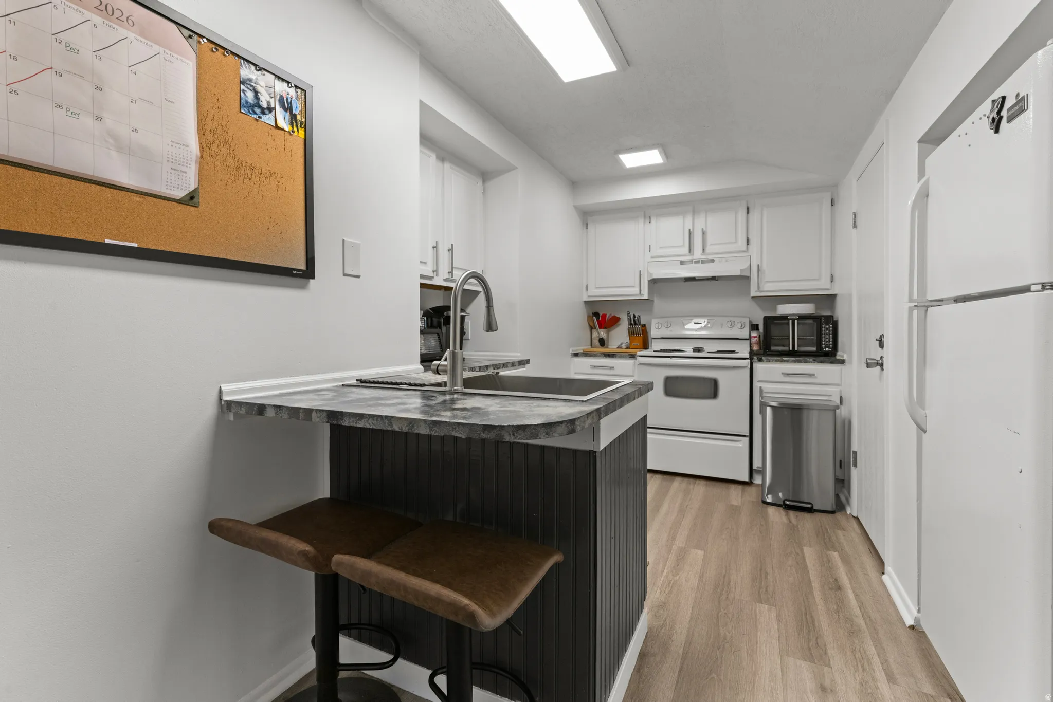 Kitchen with white cabinets, white appliances, a peninsula, dark countertops, and a breakfast bar area