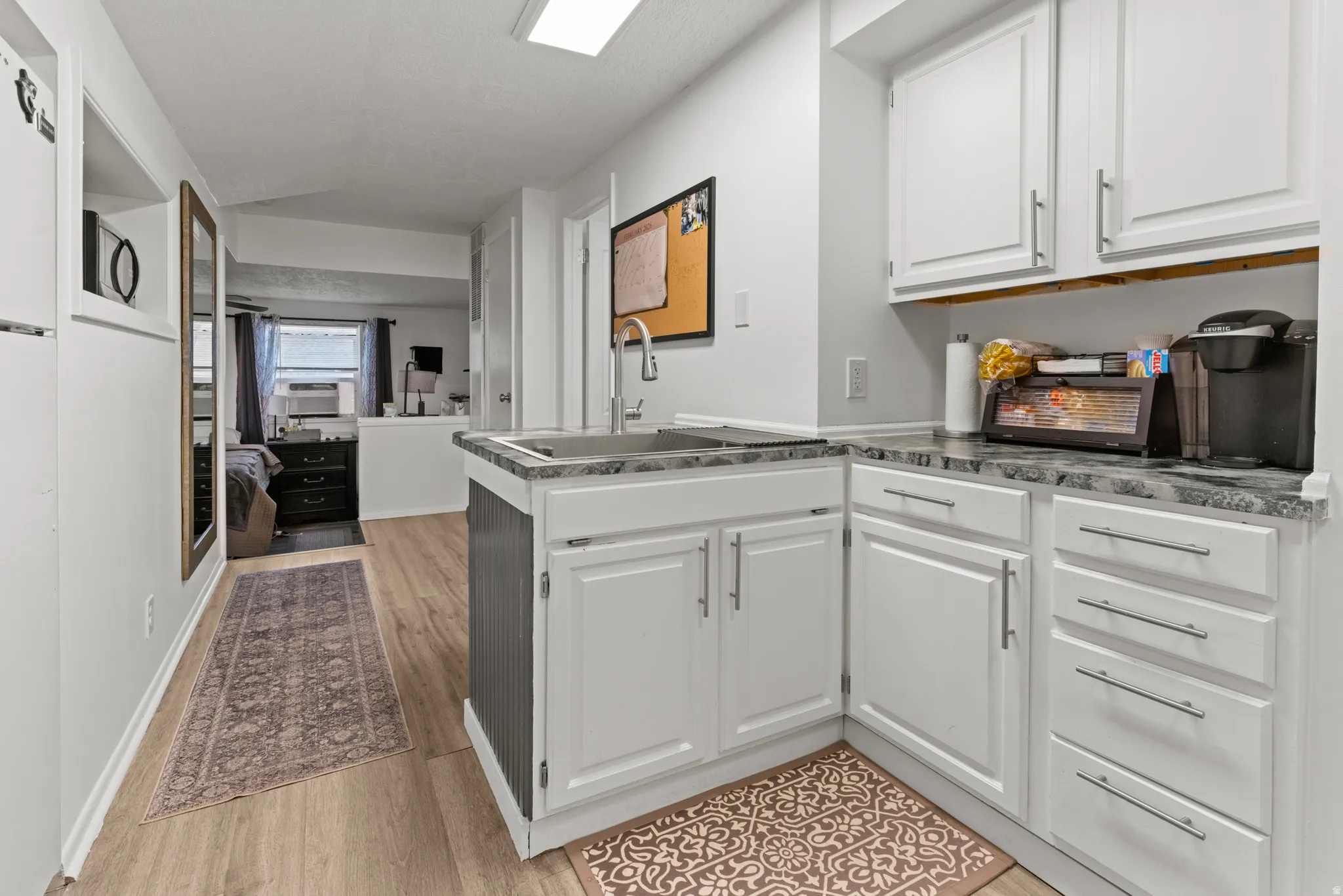 Kitchen featuring white cabinetry, open floor plan, a peninsula, light wood-style flooring, and cooling unit
