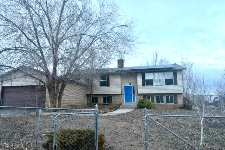 Bi-level home featuring solar panels, brick siding, a gate, a fenced front yard, and a chimney