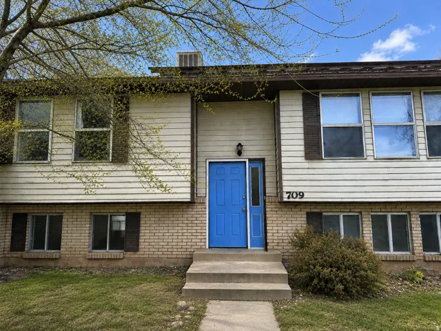 Split-level residence featuring a vibrant blue front door with a sidelight, a concrete entry staircase, and a mix of horizontal siding and brick veneer