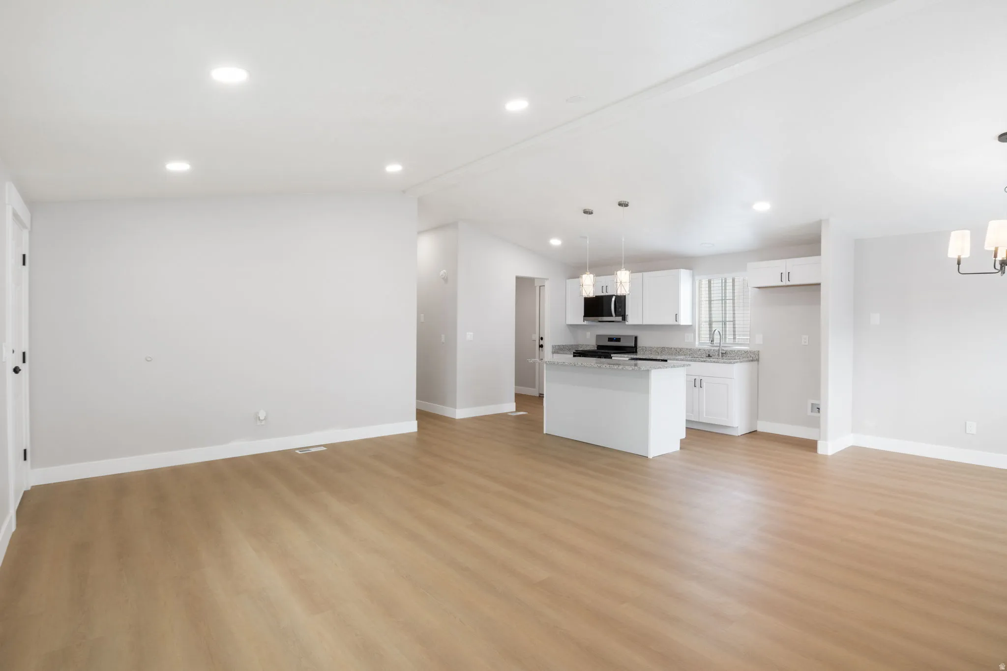 Unfurnished living room featuring light wood-style flooring and suspended lighting