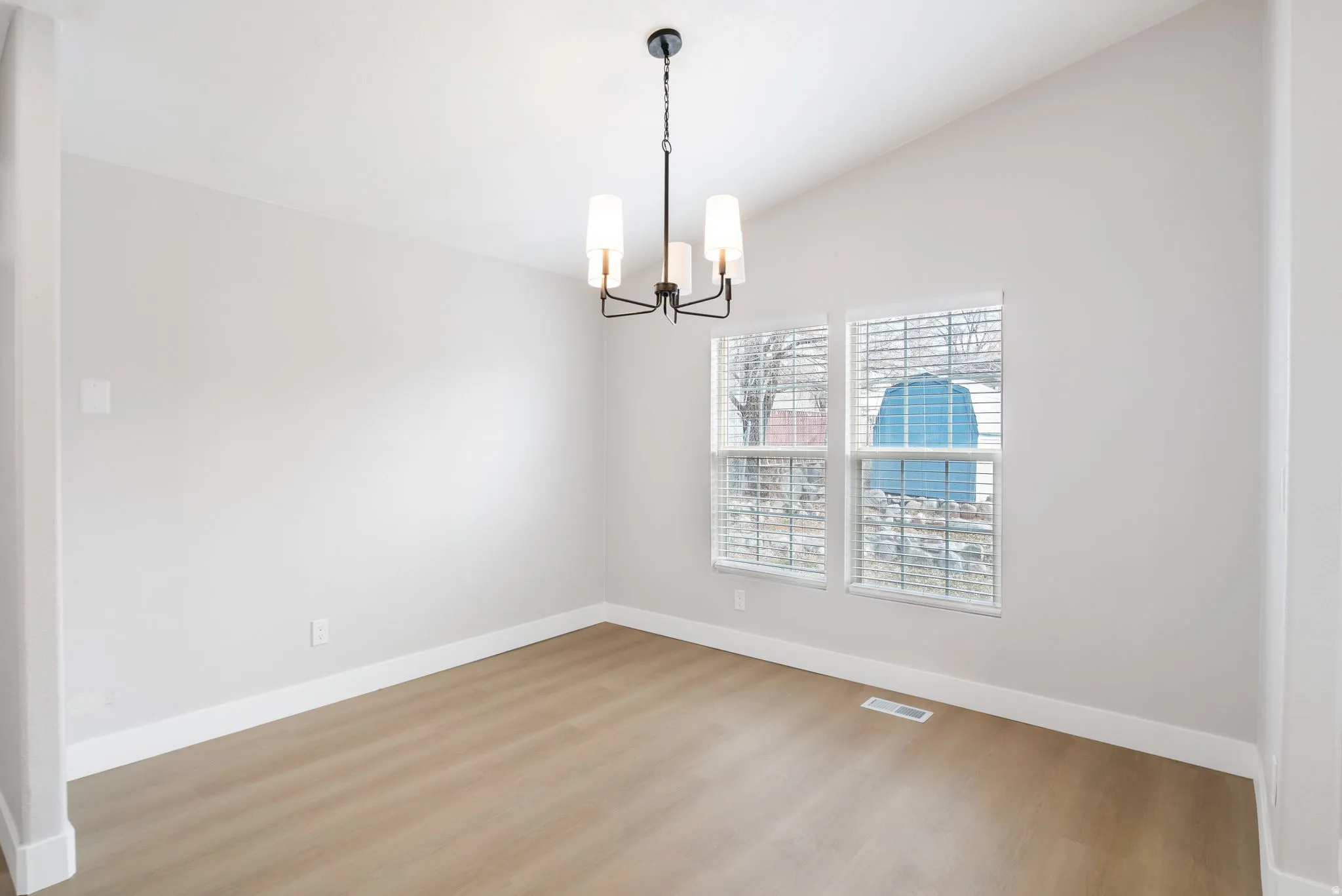 Empty room featuring wood finished floors, vaulted ceiling, and a chandelier