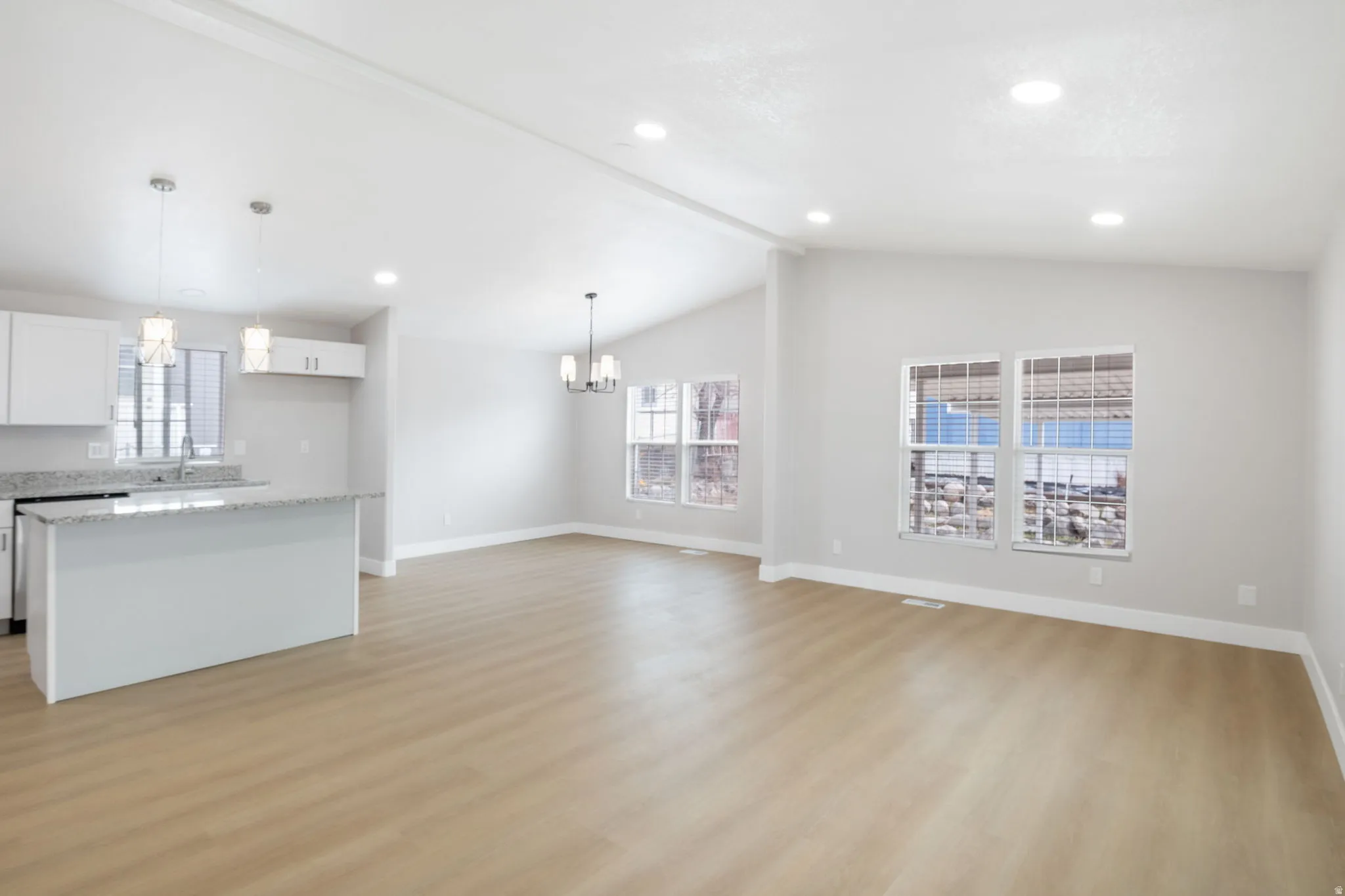 Unfurnished living room with light wood-style flooring, hanging lights, and beamed ceiling