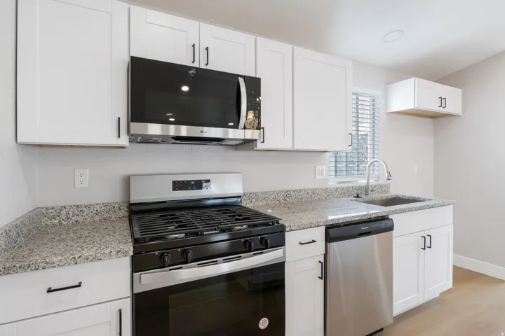 Kitchen featuring stainless steel appliances, white cabinets, light stone countertops, and light wood-style flooring