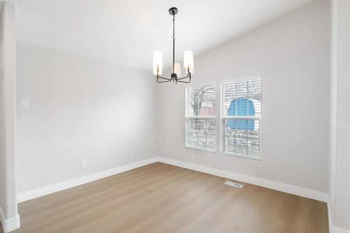 Empty room featuring wood finished floors, vaulted ceiling, and a chandelier