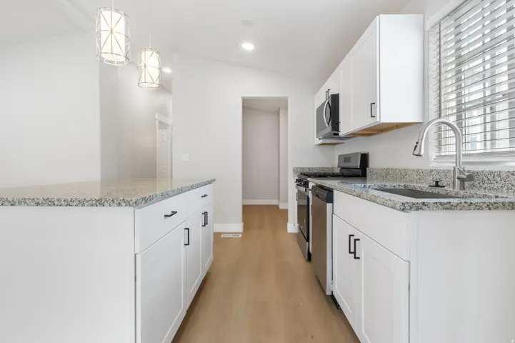 Kitchen with white cabinets, light stone counters, stainless steel appliances, vaulted ceiling, and light wood-style flooring