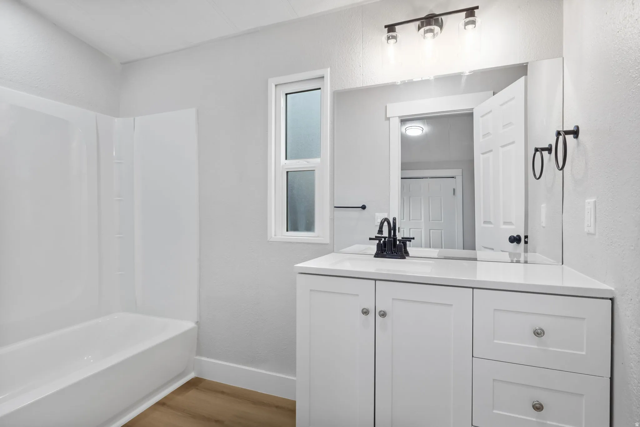 Full bath featuring a textured wall, vanity, light wood finished floors, and shower / tub combination