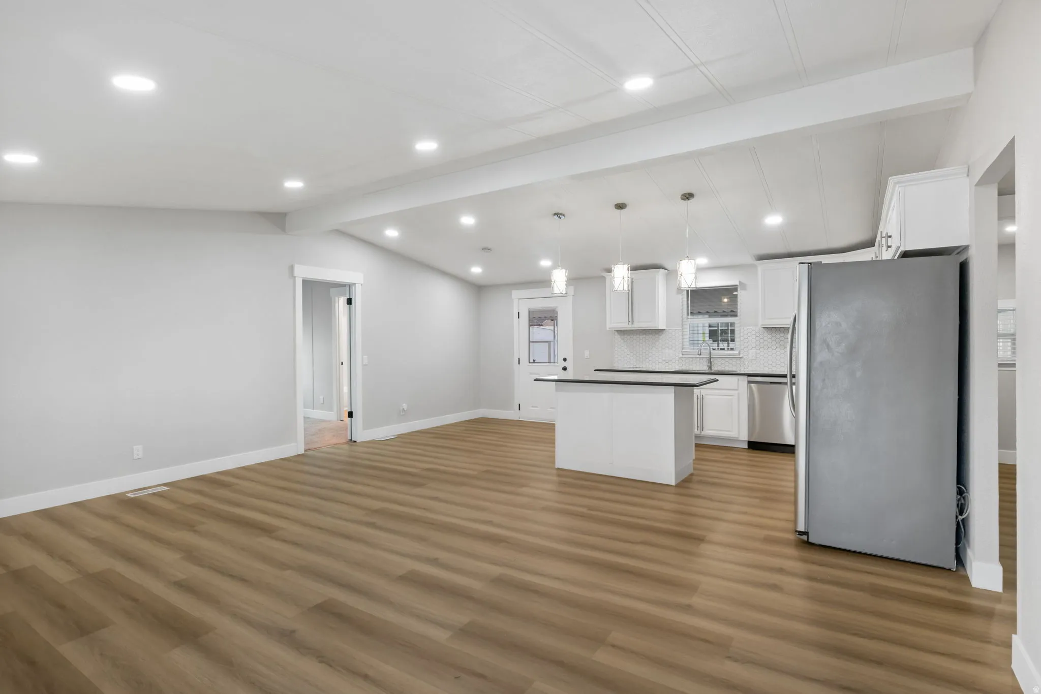 Kitchen with open floor plan, stainless steel appliances, white cabinets, beamed ceiling, and a center island