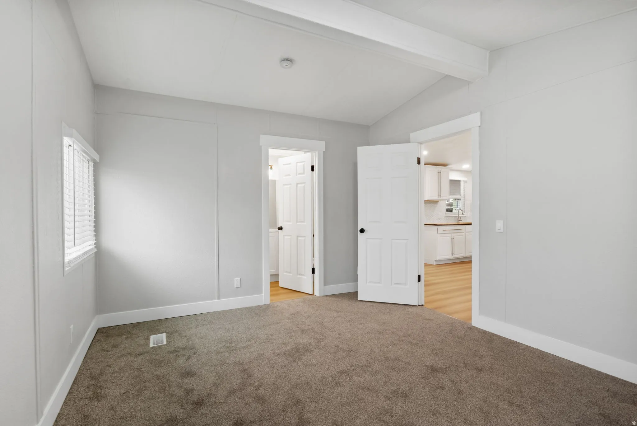Unfurnished bedroom with light colored carpet and lofted ceiling with beams