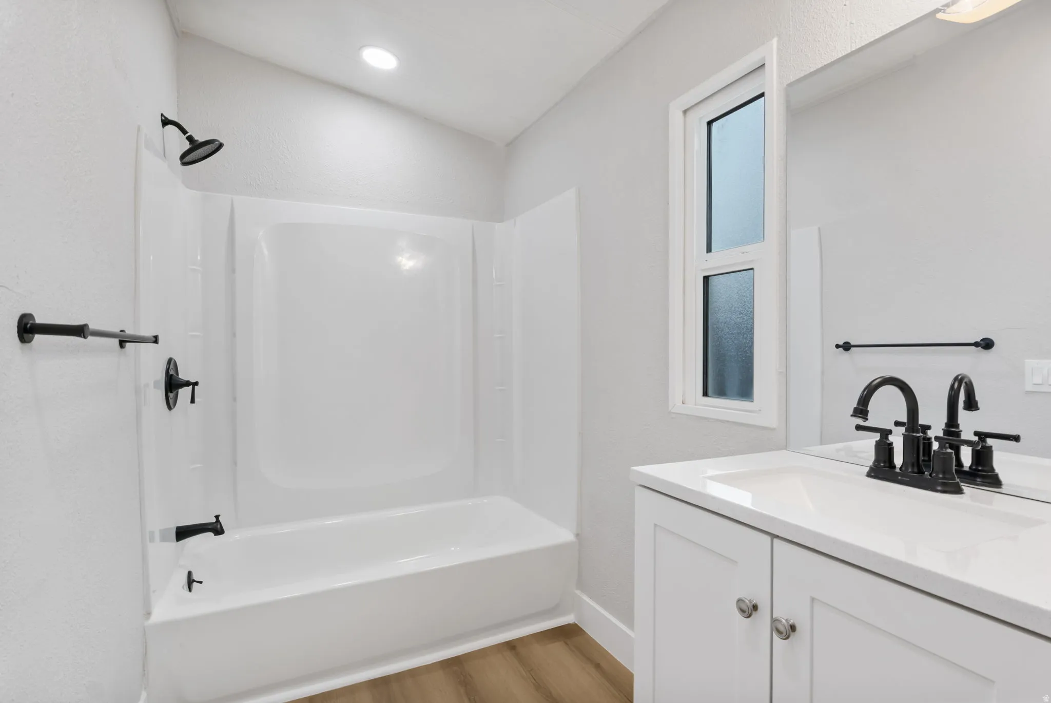 Bathroom featuring vanity, shower / washtub combination, light wood-style floors, and a textured wall