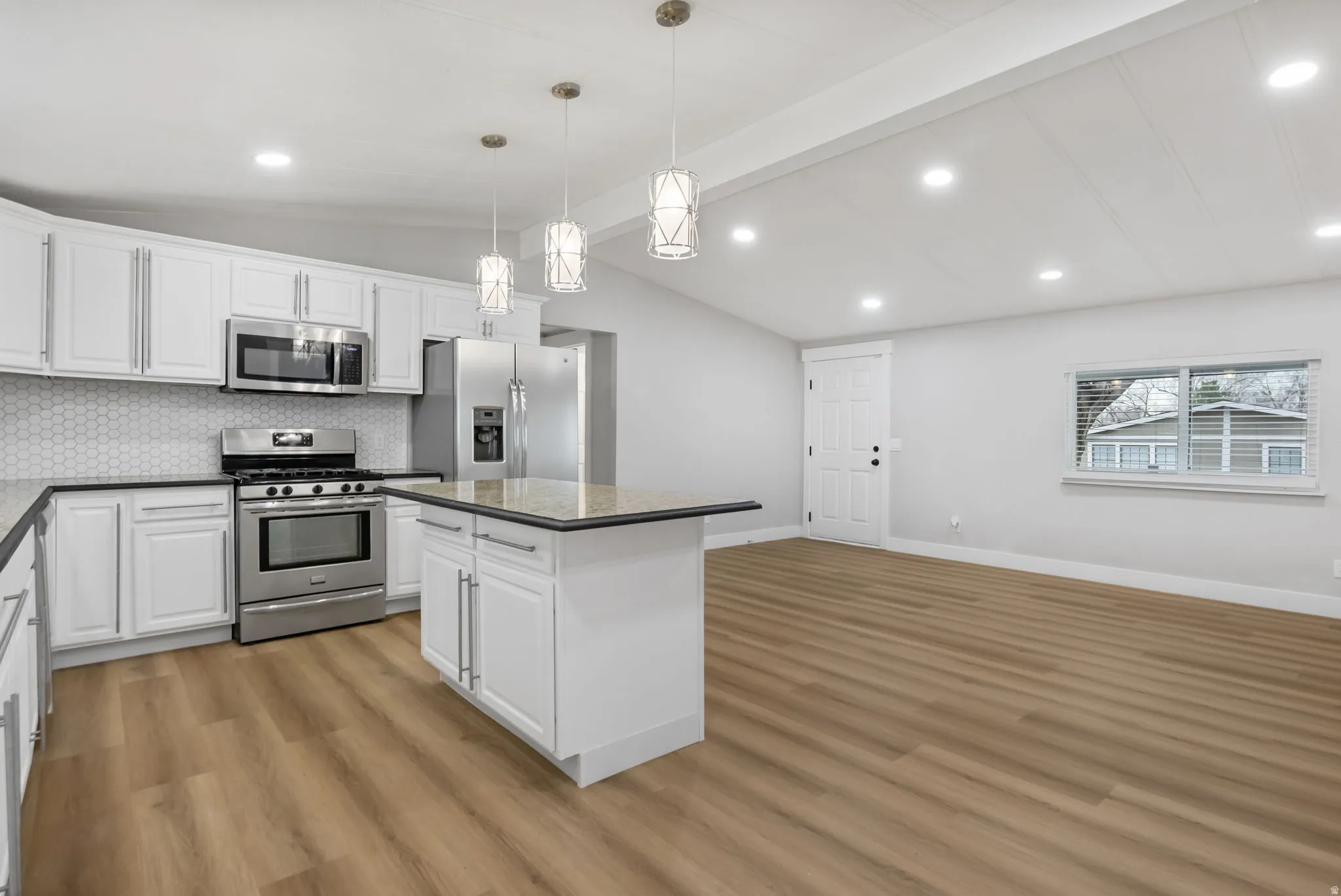 Kitchen with stainless steel appliances, white cabinets, lofted ceiling, a center island, and light wood-style floors