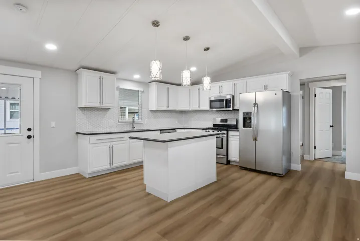 Kitchen with stainless steel appliances, hanging light fixtures, white cabinetry, light wood finished floors, and decorative backsplash