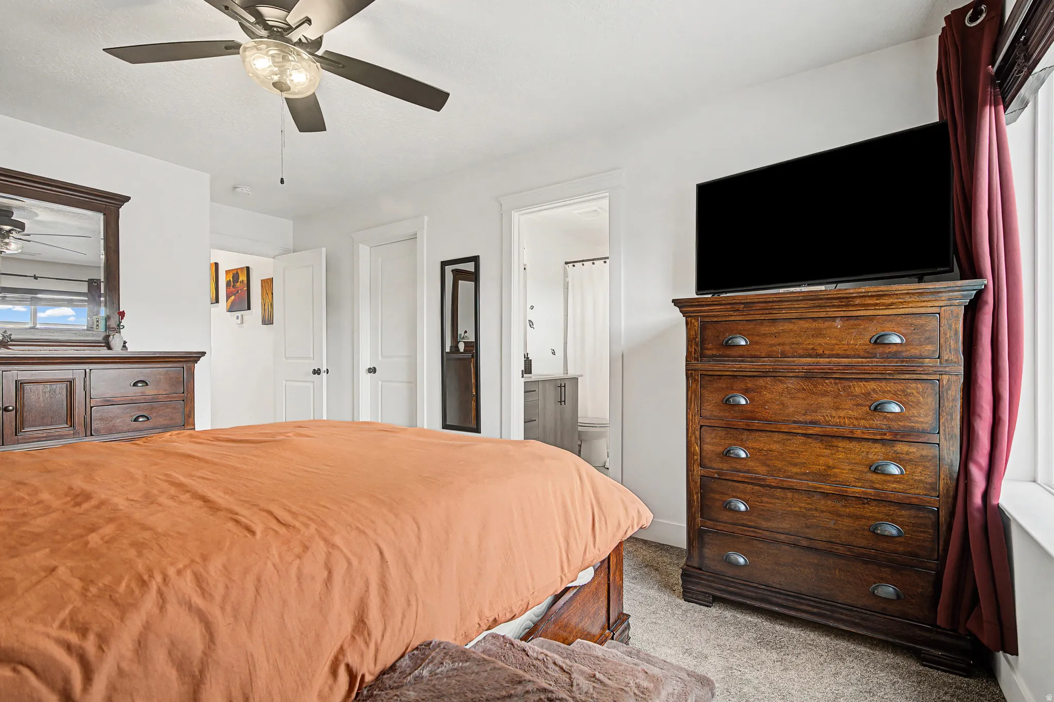 Bedroom with light colored carpet, ceiling fan, and ensuite bathroom