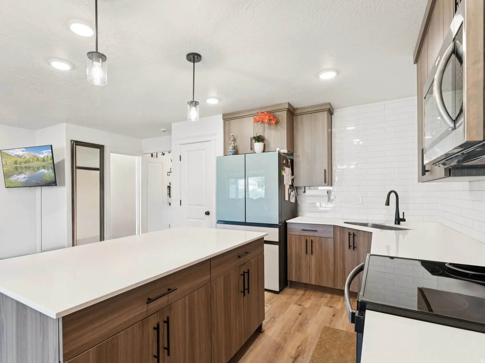 Kitchen featuring black electric range, hanging light fixtures, stainless steel microwave, light wood-type flooring, and freestanding refrigerator