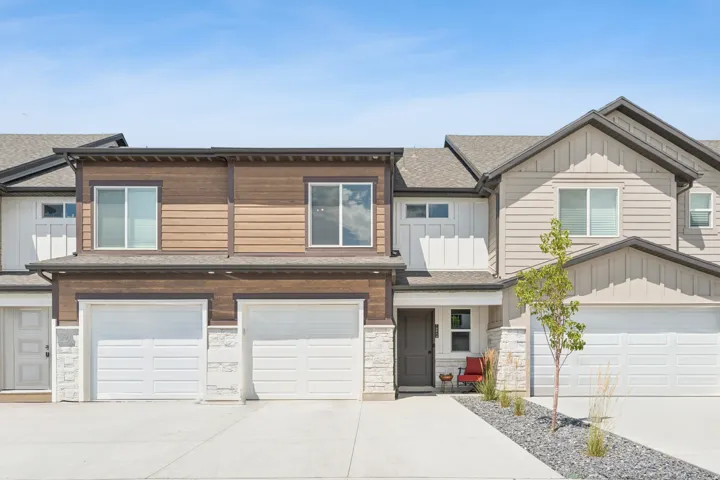 View of front facade featuring board and batten siding, driveway, a garage, roof with shingles, stone siding and space to sit in the shade