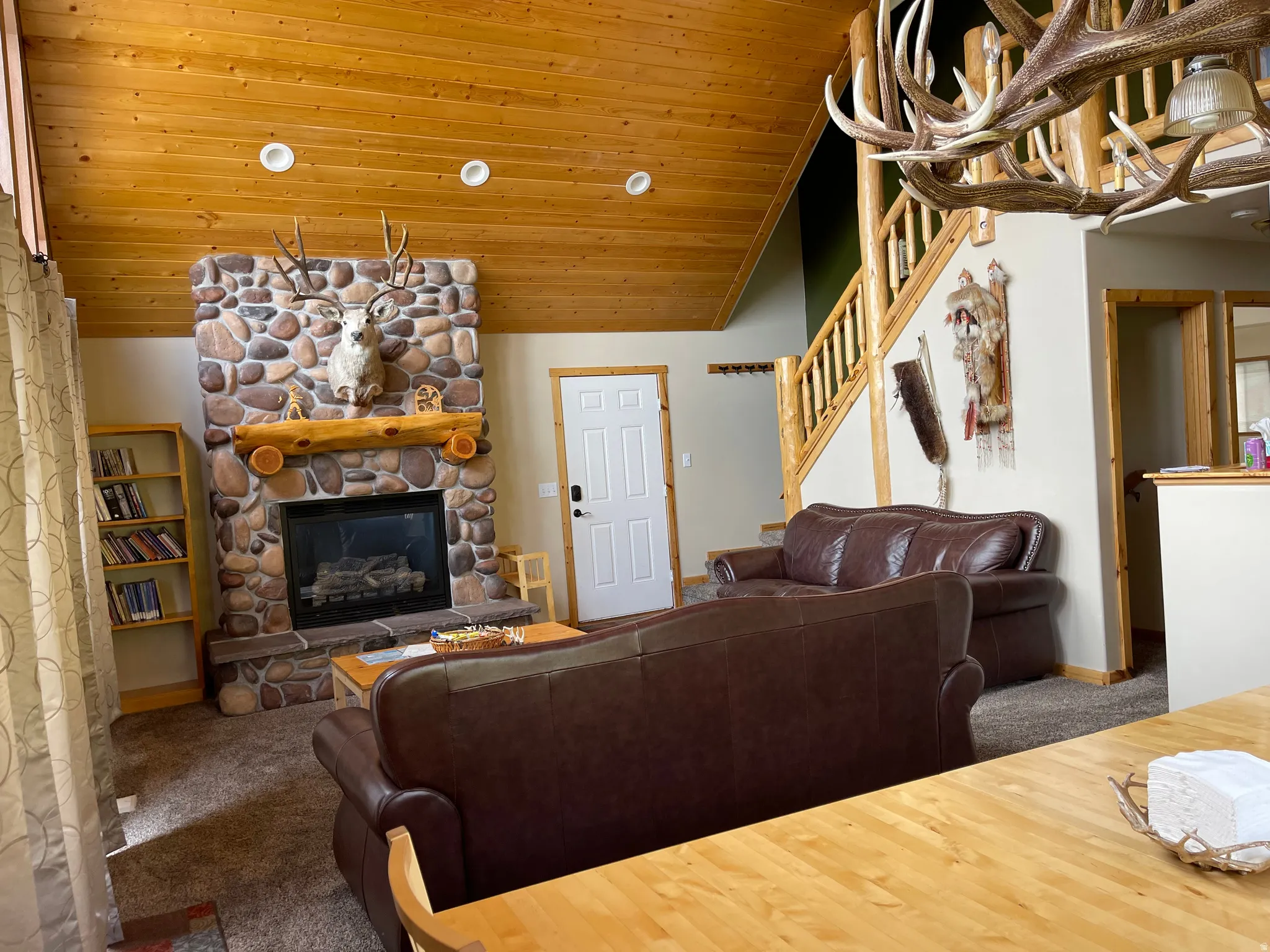 Carpeted living room featuring a stone fireplace, a vaulted wood ceiling, and hanging lights