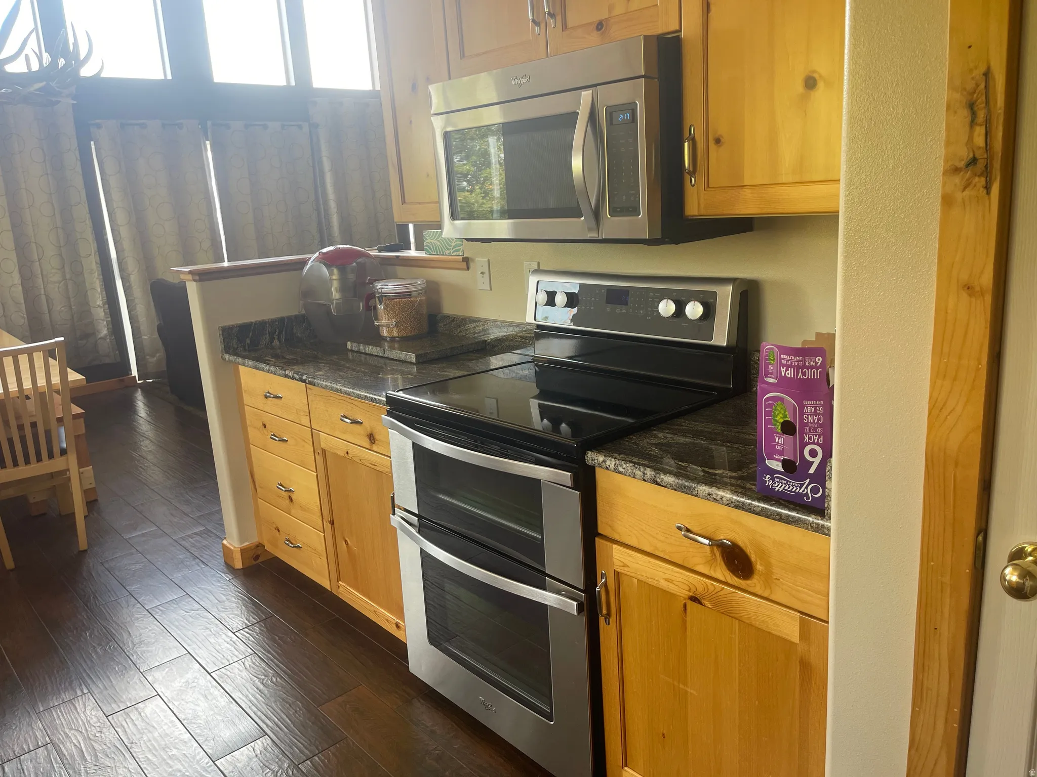 Kitchen featuring stainless steel appliances, dark wood-style flooring, dark stone countertops, and wood finish cabinets