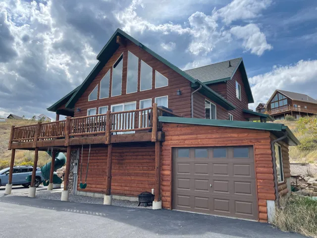 Back of house featuring faux log siding, a deck, and an attached garage