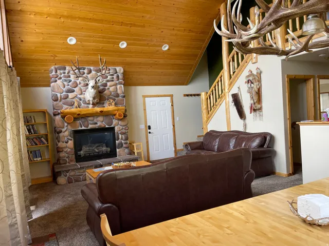 Carpeted living room featuring a stone fireplace, a vaulted wood ceiling, and hanging lights