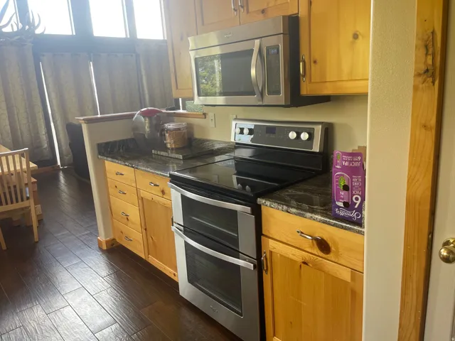 Kitchen featuring stainless steel appliances, dark wood-style flooring, dark stone countertops, and wood finish cabinets