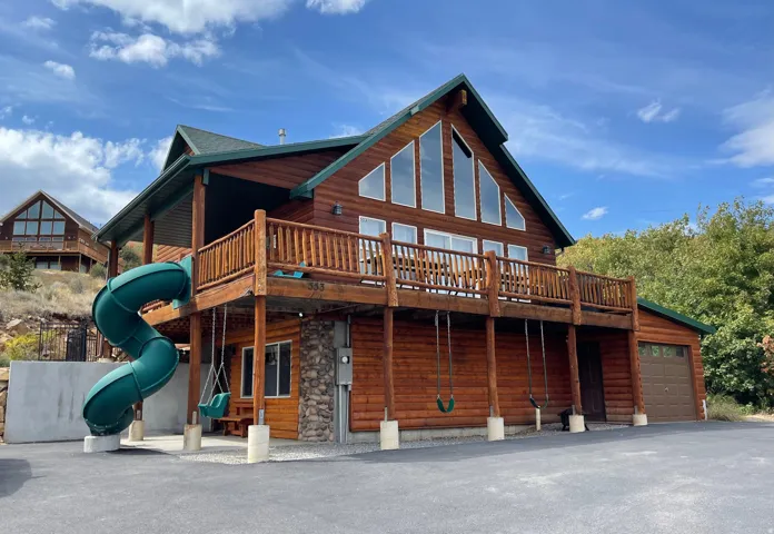 Back of house with a wooden deck, faux log siding, and stone siding