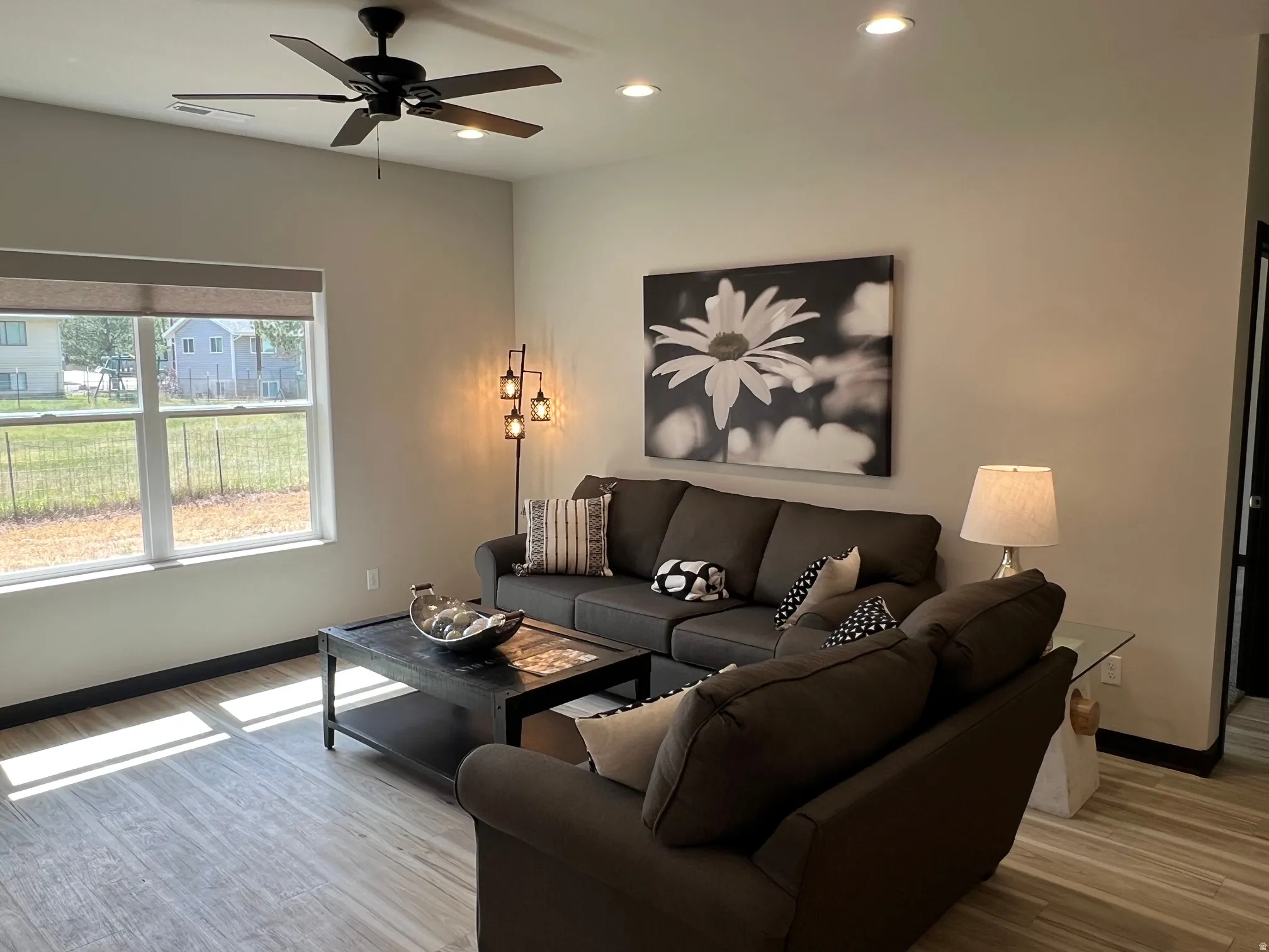 Spacious living area featuring wood-finish flooring, a large window with roller shades, a ceiling fan, and recessed lighting