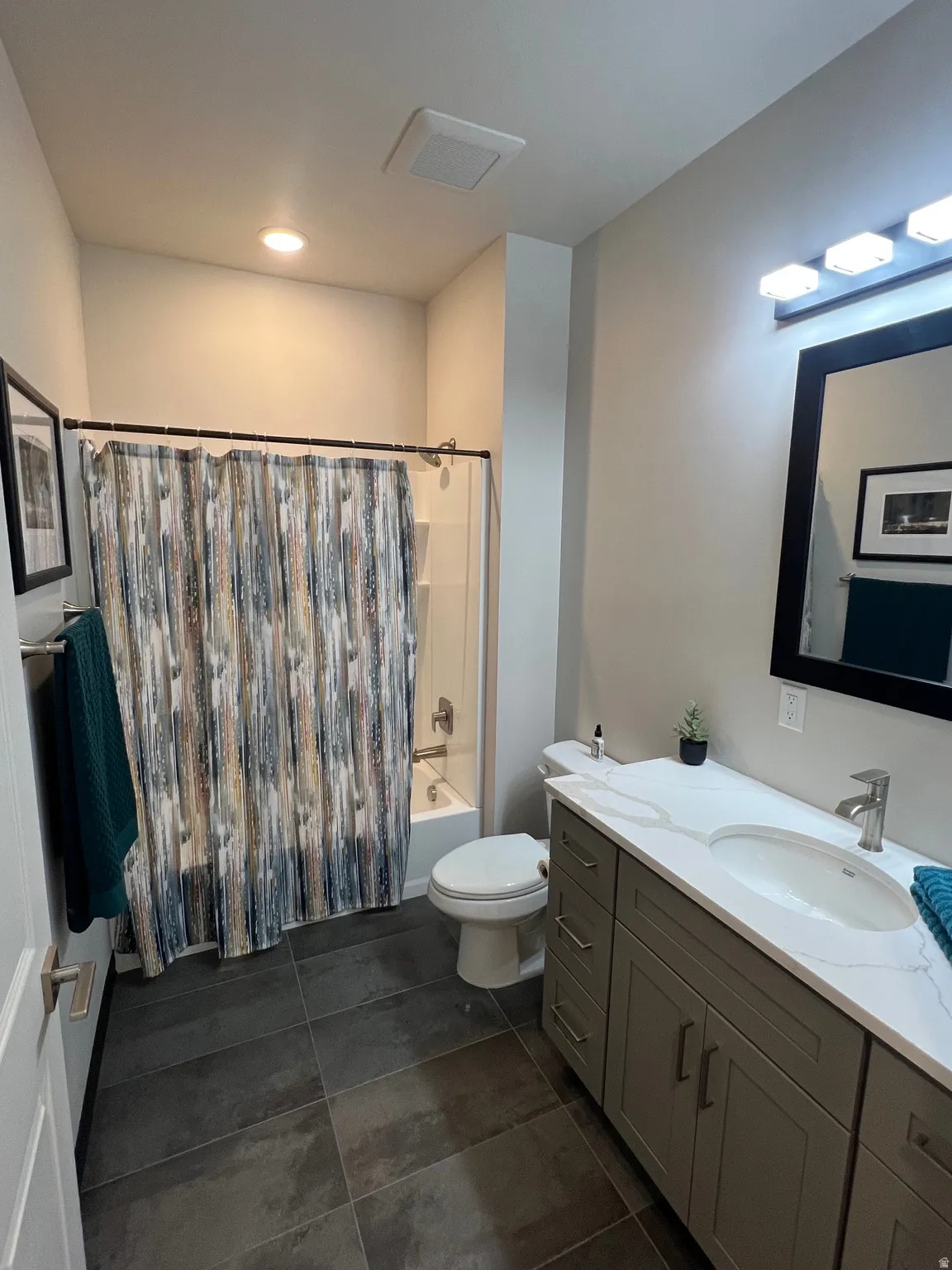 Full bathroom featuring a single shower-tub combination, a toilet, a vanity with double sinks, and dark tile flooring