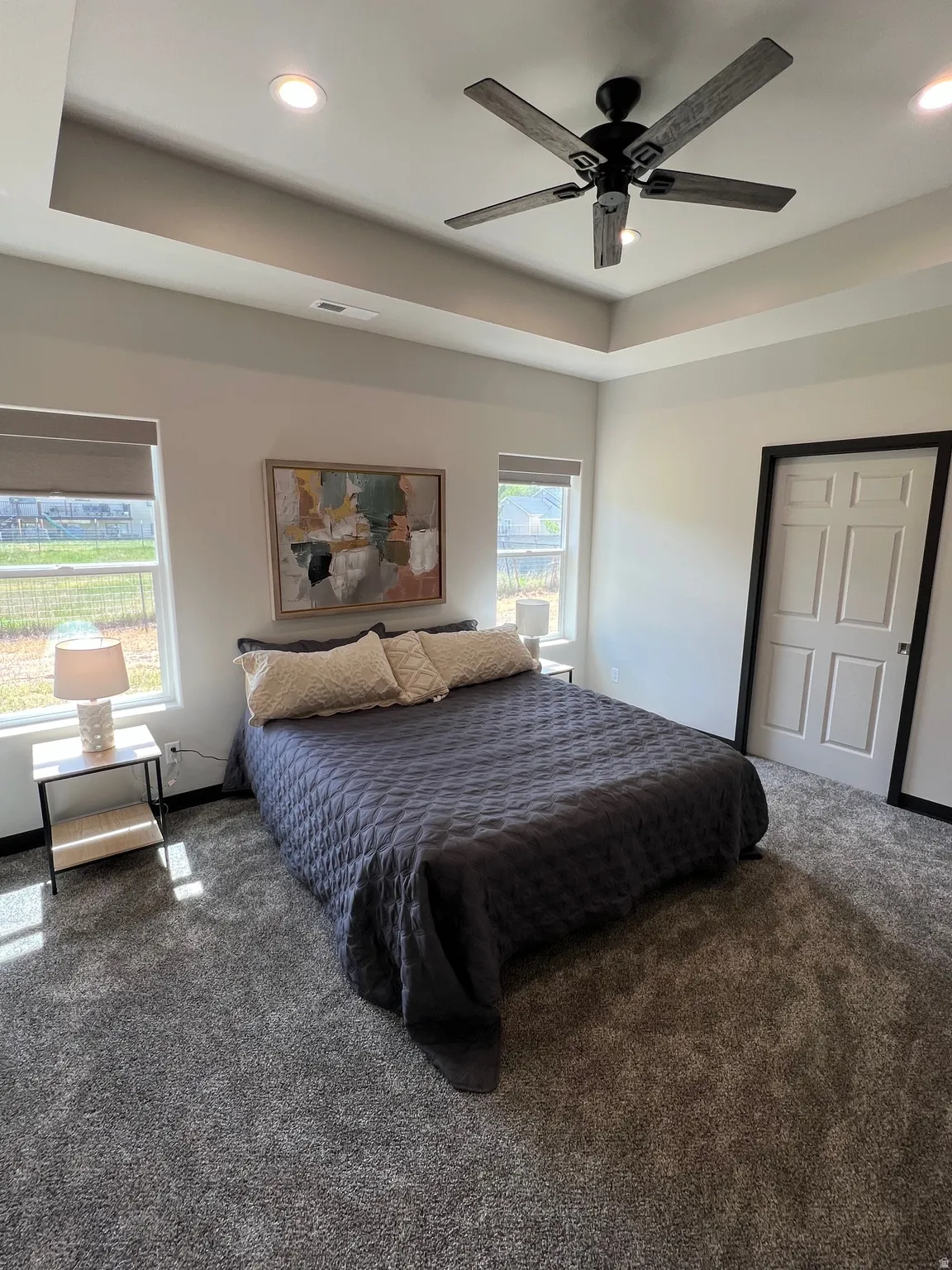 Spacious room featuring a tray ceiling with recessed lighting and a ceiling fan, two windows with blinds, and plush carpeting