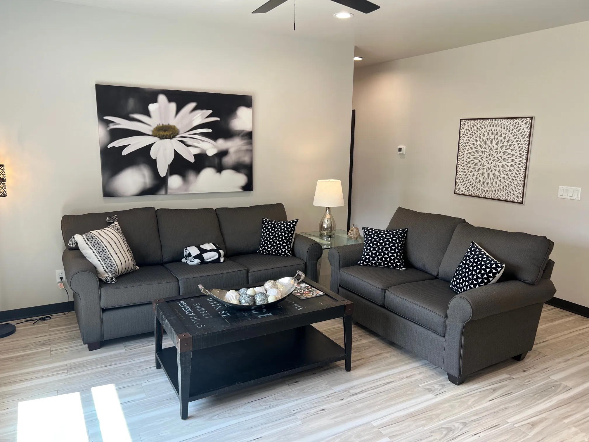 Spacious living area featuring light-toned walls, wood-finish flooring, and a ceiling fan
