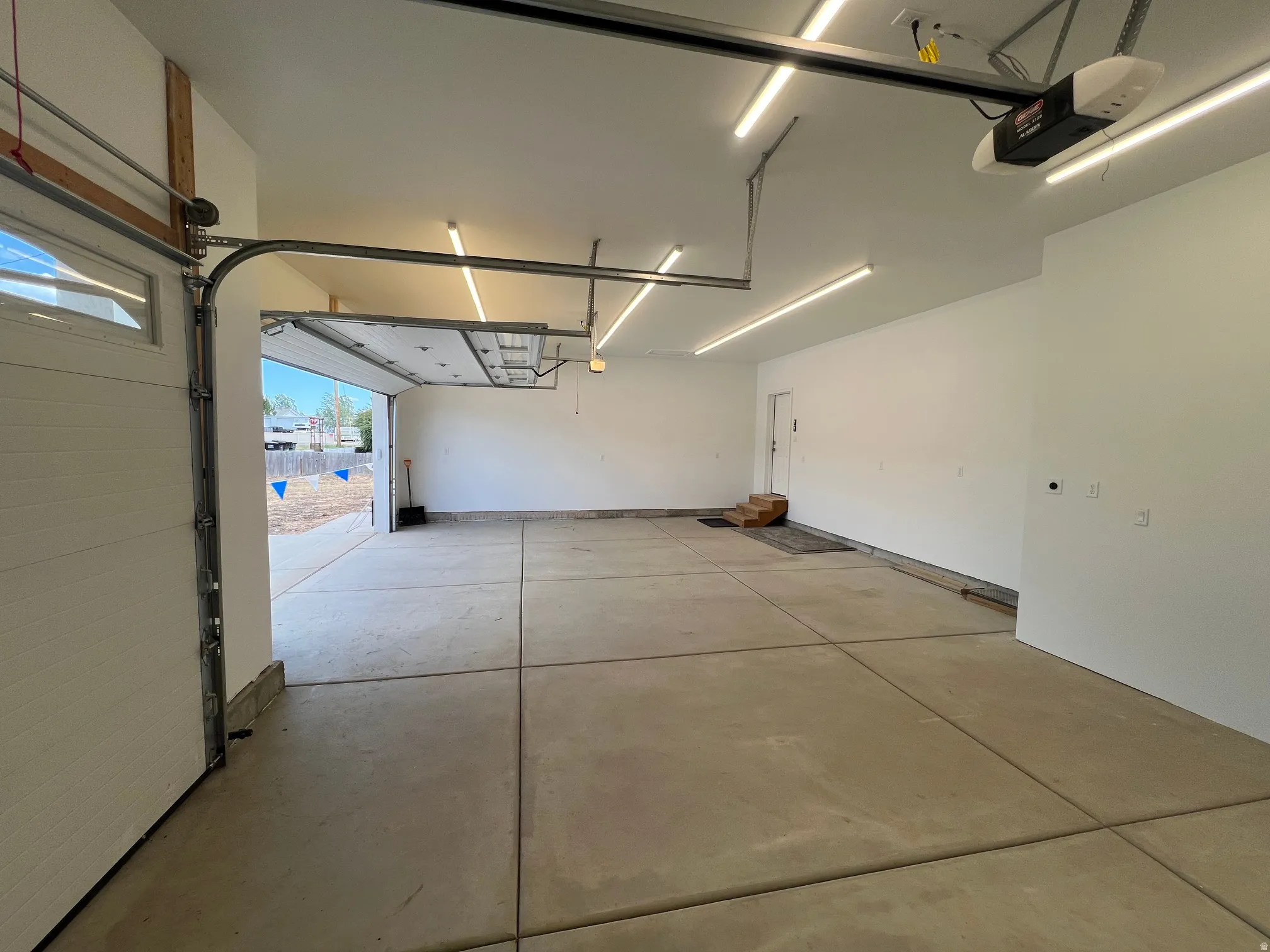 Spacious garage featuring a sectional overhead door with window inserts, concrete flooring, automatic garage door opener, multiple linear ceiling light fixtures, and a side entry door