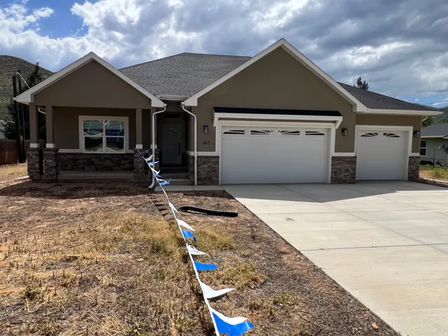 Contemporary ranch-style residence featuring a prominent two-car garage, stone veneer accents, stucco exterior finish, and a covered entryway