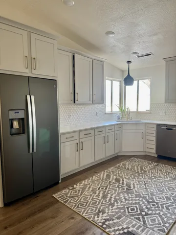 Kitchen with stainless steel appliances, dark wood finished floors, backsplash, and light stone countertops