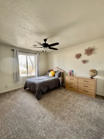 Carpeted bedroom with a textured ceiling and ceiling fan