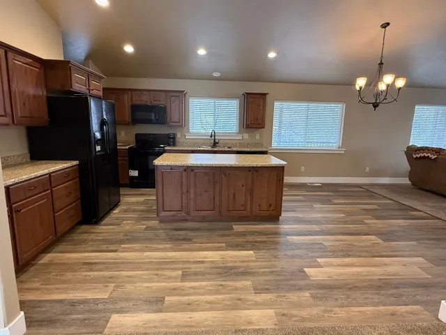 Kitchen with vaulted ceiling, black appliances, a chandelier, a kitchen island, and dark wood-type flooring