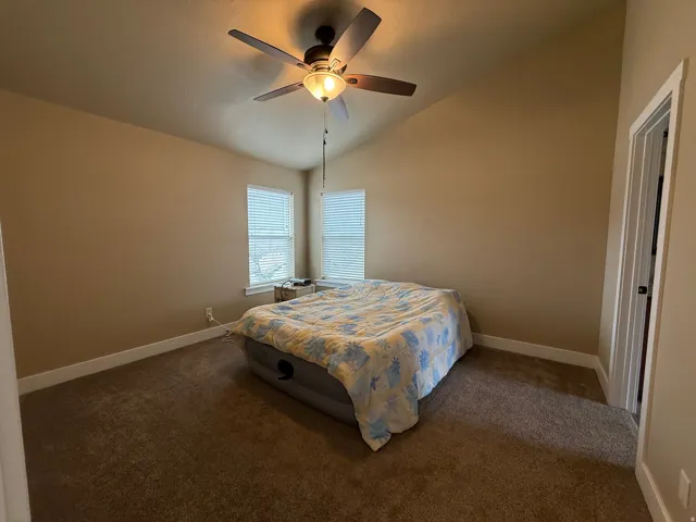 Carpeted bedroom featuring vaulted ceiling and a ceiling fan