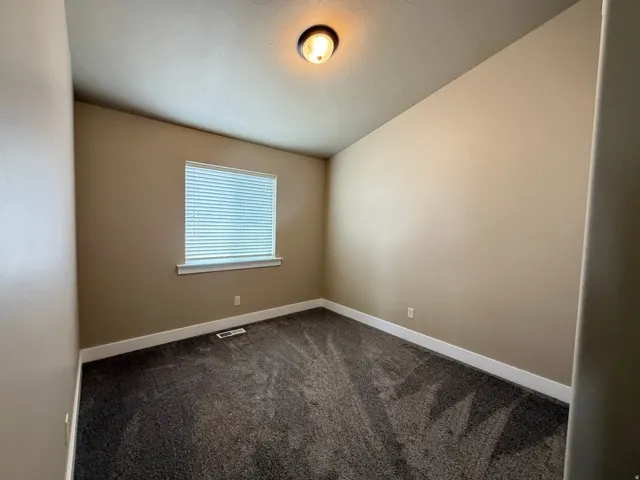 Spare room with dark colored carpet and vaulted ceiling