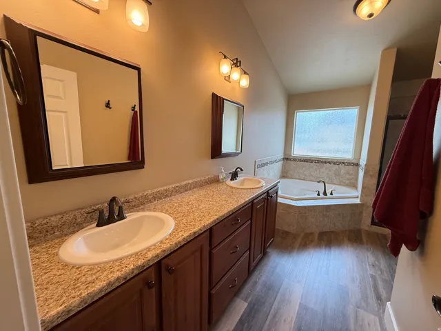 Full bath featuring double vanity, dark wood finished floors, a garden tub, and vaulted ceiling