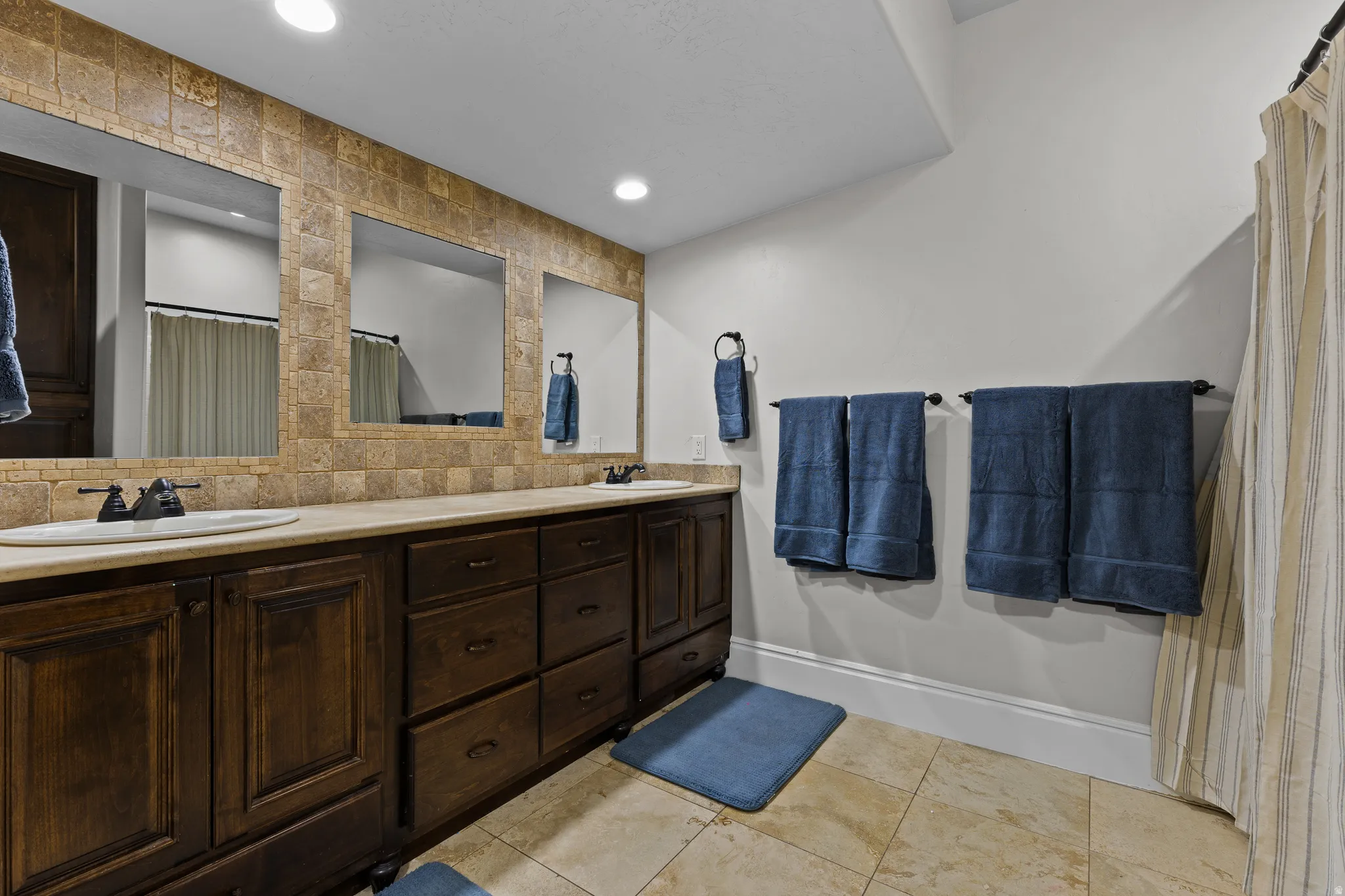 Bathroom featuring double vanity, decorative backsplash, a shower with shower curtain, and recessed lighting