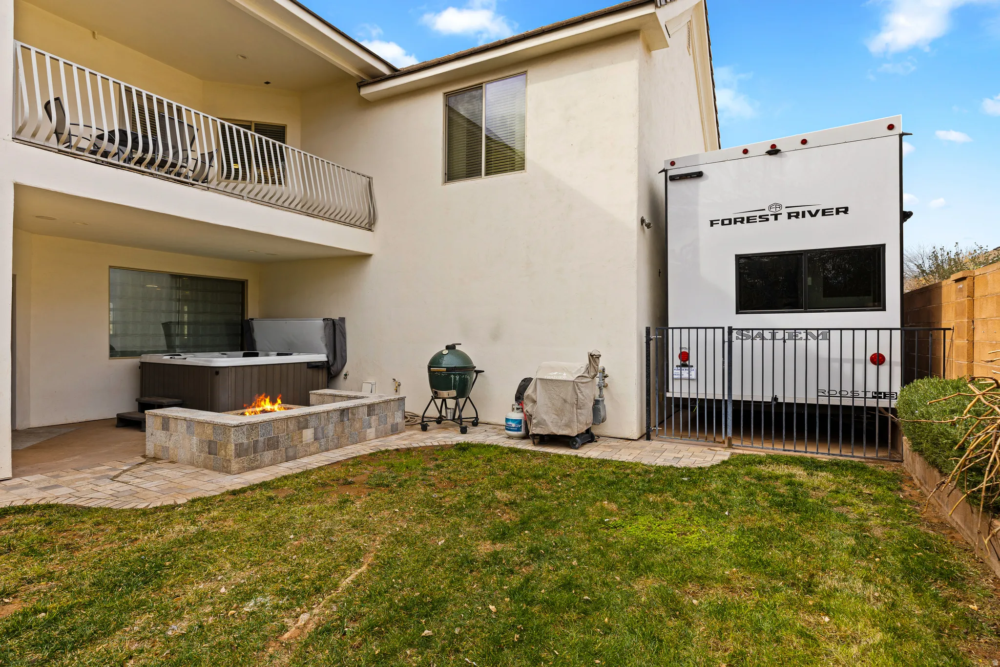 Rear view of house with a balcony, a patio area, stucco siding, and an outdoor fire pit