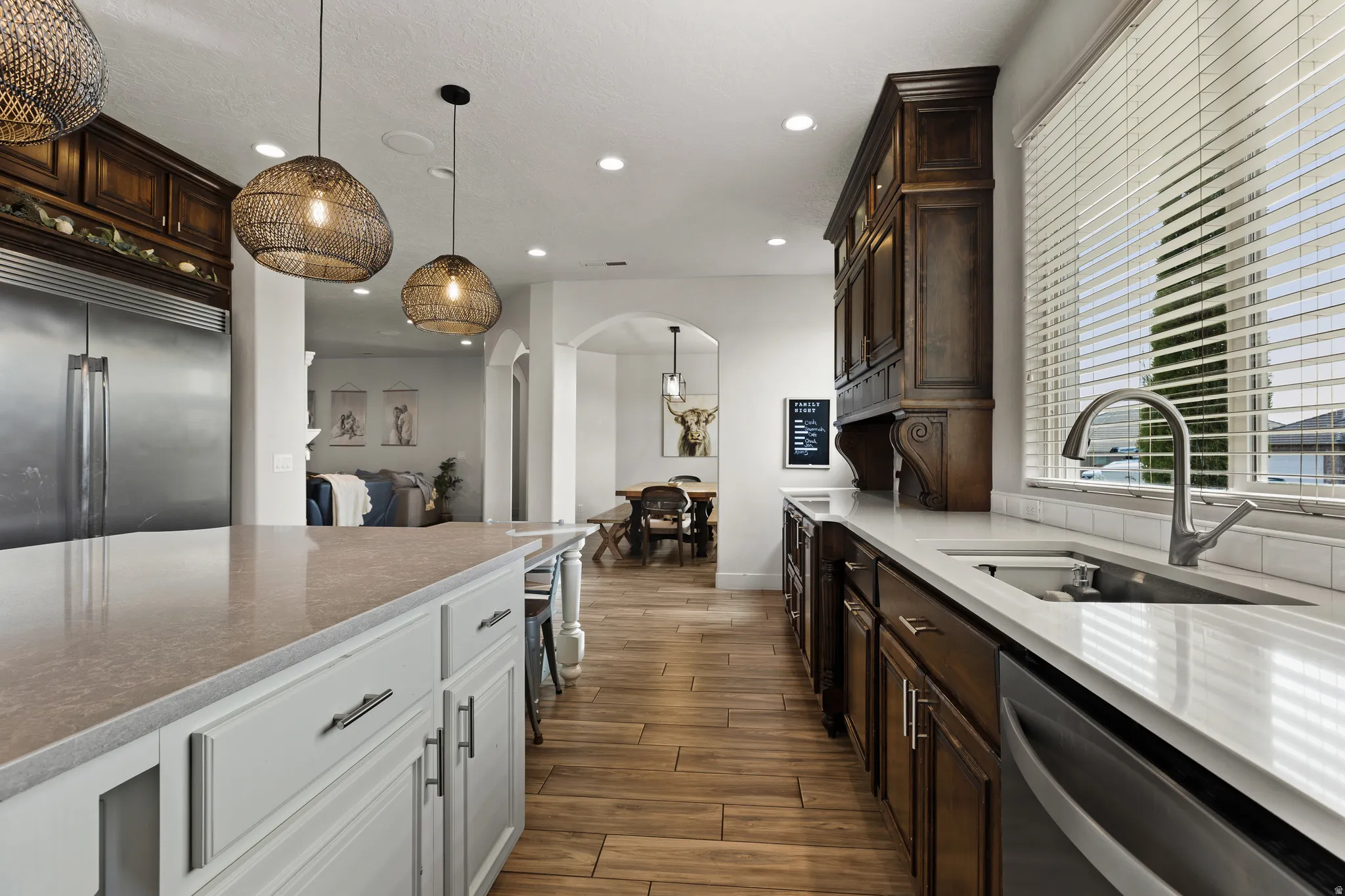 Dual tone kitchen with light stone counters, decorative light fixtures, arched walkways, wood finish floors, and two tone cabinetry