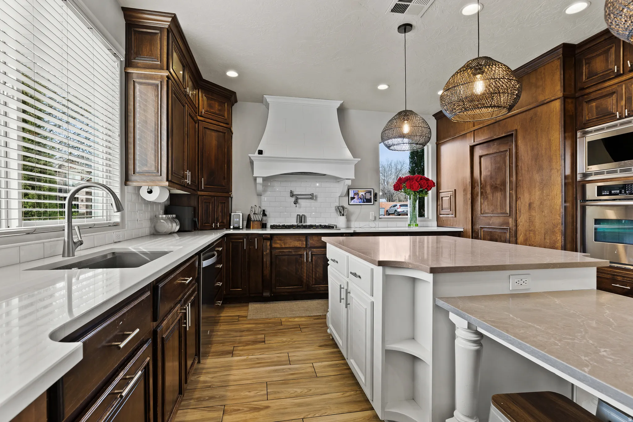 Kitchen featuring two tone color scheme, light wood-type flooring, hanging light fixtures, stainless steel appliances, and decorative backsplash