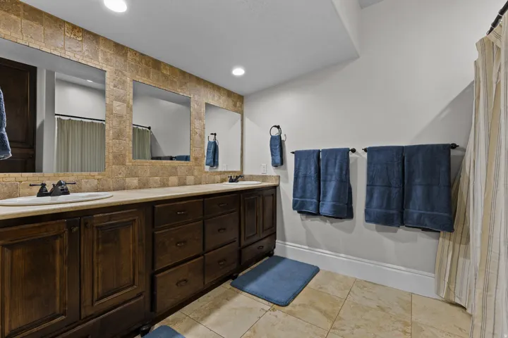 Bathroom featuring double vanity, decorative backsplash, a shower with shower curtain, and recessed lighting