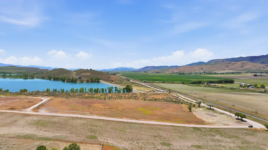 Expansive landscape featuring a body of water with surrounding foliage, open fields, and distant mountains