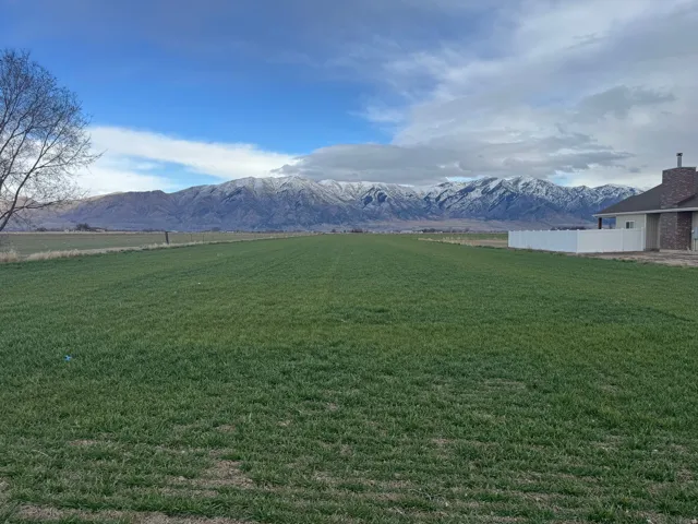 Expansive green field with mountain backdrop, partial brick exterior, and white privacy fence