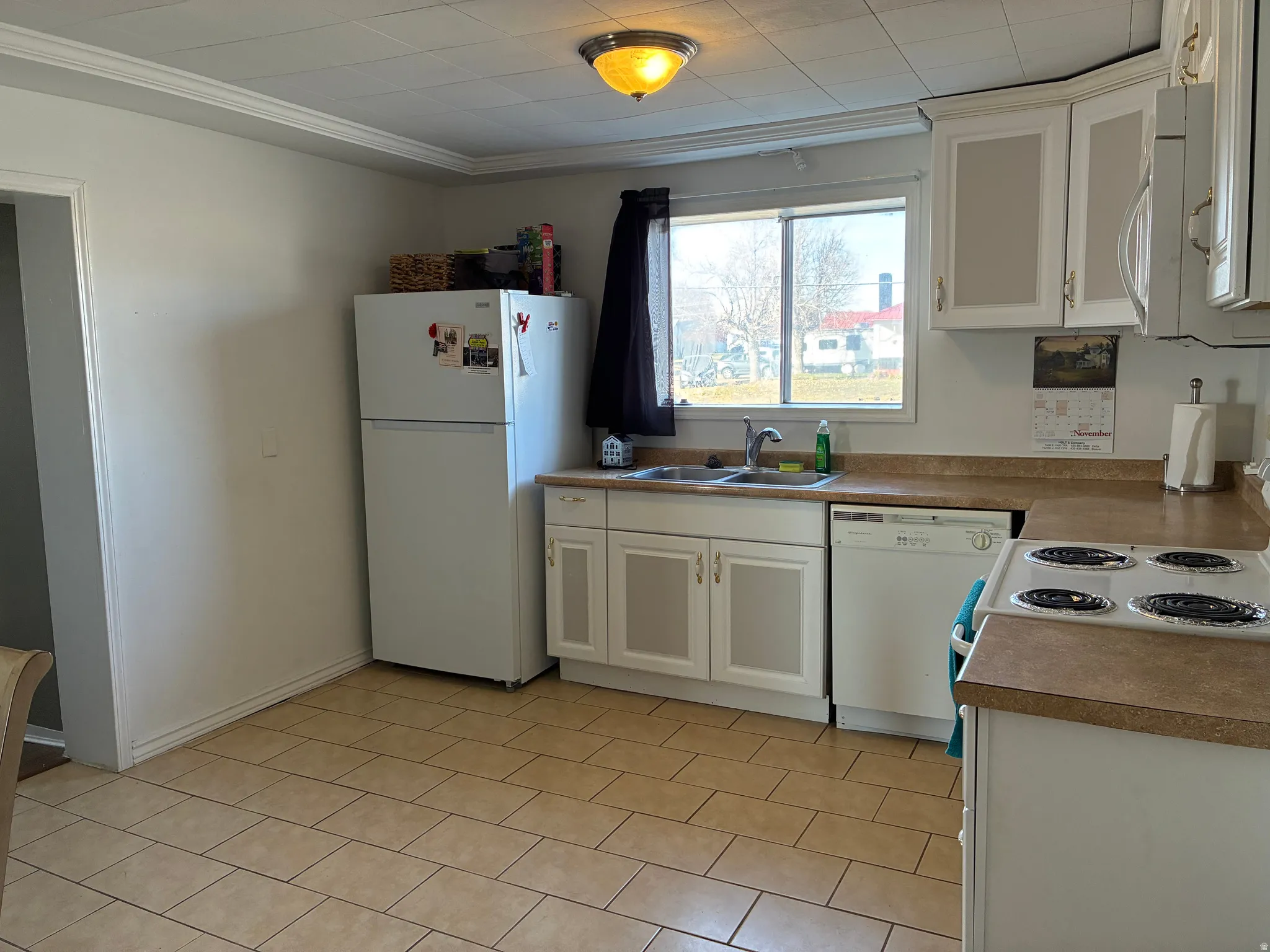 Kitchen with white cabinets, white appliances, ornamental molding, and light countertops