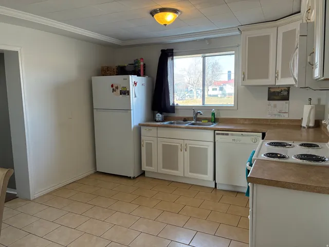 Kitchen with white cabinets, white appliances, ornamental molding, and light countertops